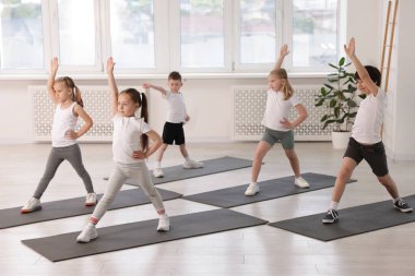 Sınıftaki minderler üzerinde yoga yapan bir grup çocuk.