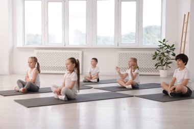 Sınıftaki minderler üzerinde yoga yapan bir grup çocuk.