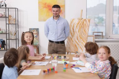 Çocuklara resim dersinde resim yapmayı öğreten bir adam.