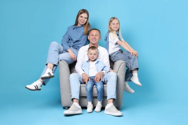 Mutlu aile, açık mavi arka planda koltukta oturuyor.