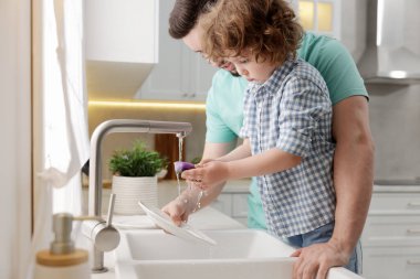 Baba ve oğlu evde birlikte bulaşık yıkıyorlar.