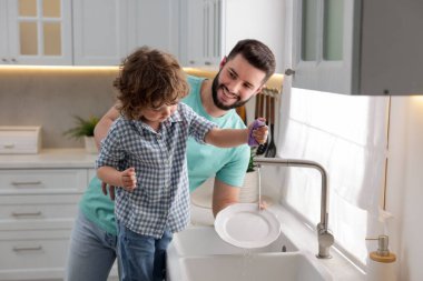 Baba ve oğlu evde birlikte bulaşık yıkıyorlar.