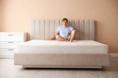 Genç adam evinde yumuşak bir yatakla yatakta oturuyor.