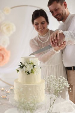 Evli çift evde bıçakla düğün pastası kesiyor, seçici bir odak noktası var.