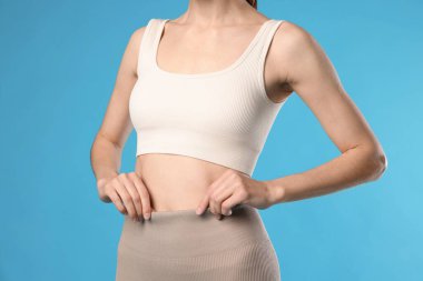 Açık mavi arka planda düz göbekli güzel bir kadın, yakın plan.