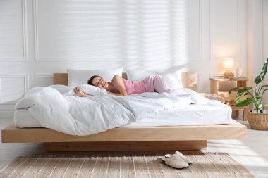 Evde yumuşak bir şilteyle yatakta uzanan bir kadın.