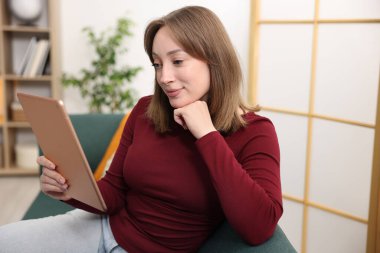Evdeki koltukta modern tabletli bir kadın.