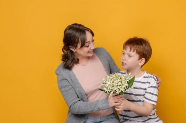 Çocuk sarı arka planda annesine güzel bir çiçek buketi veriyor.