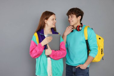 Gri arka planda sırt çantası ve dizüstü bilgisayarı olan gençler.