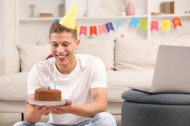 Pastalı bir adam doğum gününü kutluyor ve evde bilgisayarla video görüşmesi yapıyor.