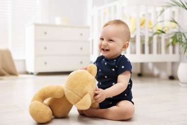 Küçük şirin bebek odada oyuncak ayıyla oynuyor.