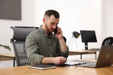 Ofiste masa başında çalışan bir adam telefonda konuşuyor.