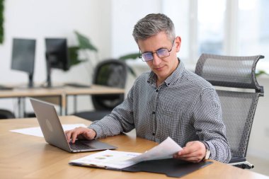 Ofiste evrak ve dizüstü bilgisayarla çalışan bir işadamı.