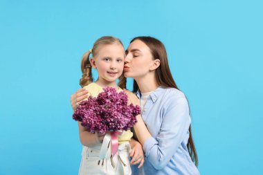 Anne ve kızı açık mavi arka planda bir demet leylak çiçeğiyle