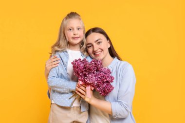 Anne ve kızı sarı arka planda bir demet leylak çiçeğiyle