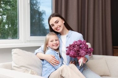 Anne ve kızı evde bir buket leylak çiçekleriyle