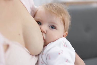 Anne küçük bebeğini evde emziriyor, yakın plan.