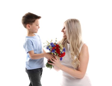 Küçük çocuk, gülümseyen annesine beyaz arka planda bir buket güzel çiçek sunuyor.