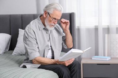 Görme sorunu olan son sınıf öğrencisi evde yatağında kitap okuyor.