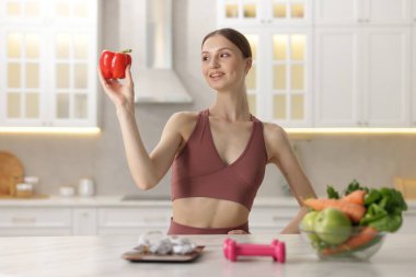 Mutfak terazili biber tutan kadın, mezura, halterler ve evde sağlıklı yiyecekler.