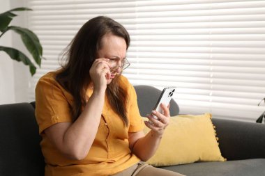 Görme sorunu olan bir kadın evdeki koltukta akıllı telefon kullanıyor, mesaj atmak için yer var.