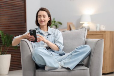 Evdeki koltukta modern akıllı telefon kullanan bir kadın.