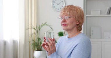 Yaşlı kadın evde camdan su içiyor.