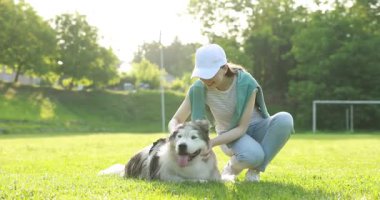 Gülümseyen kadın sabahın köründe yeşil çimlerin üzerinde sevimli Alaska köpeğini okşuyor ve ona sarılıyor.