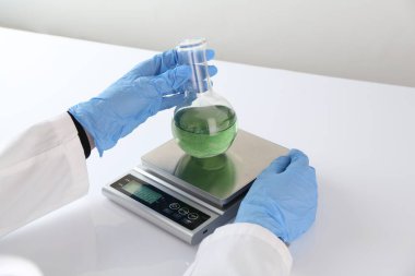Bilim adamı beyaz masadaki terazide numune tartıyor, yakın plan.