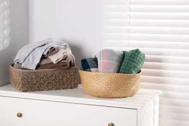 Beyaz komodinin üstündeki sepetlerde yün kazaklar ve eşarplar.