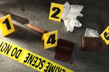 Adli tıp uzmanı. Sarı suç mahalli bandı, işaretler ve kanıtlar gri masada, üst tarafta.