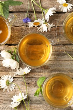 Cam bardaklarda Aromatik bitki çayı, çiçekler ve yeşil yapraklar ahşap masada, düz uzanmış