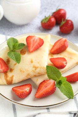 Çilekli leziz krepler ve açık gri masada nane şekeri, yakın plan.