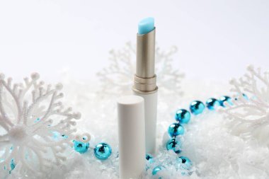 Nemlendirici dudak kremi ve yapay kar üzerine Noel süsü, yakın plan. Kış bakımı
