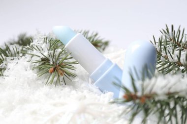 Nemlendirici dudak kremi ve suni kar üzerinde köknar ağacı dalları, yakın plan. Kış bakımı