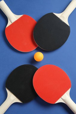 Masa tenisi raketleri ve top mavi arka planda, düz yatıyordu.