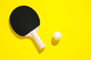 Sarı arka planda pinpon raketi ve top, üst manzara. Metin için boşluk