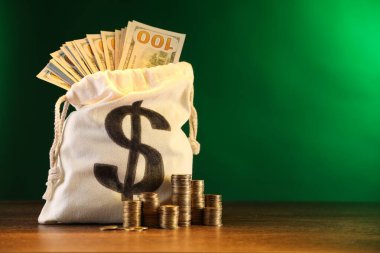 Dolar banknotları ve ahşap masaya yığılmış bozuk paralarla dolu çanta yeşil eğimli arka plan, metin için boşluk
