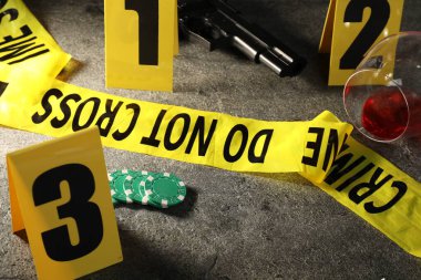 Adli tıp uzmanı. Sarı olay yeri bandı, keçeli kalem, poker fişi, silah ve bardak şarap gri masada, yakın plan.