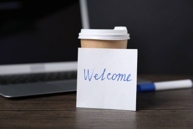 Kelimesi kelimesine kağıt not Hoş geldin, bir fincan kahve, kalem ve dizüstü bilgisayar ahşap masada