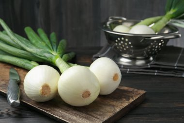Taze taze soğanlar, kesme tahtası ve bıçakla siyah ahşap masa, yakın plan.