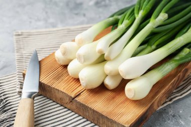 Taze taze soğanlar, kesme tahtası ve bıçakla gri desenli masa, yakın plan.