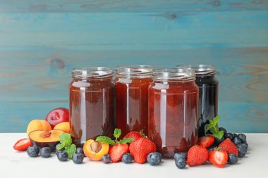 Kavanozlardaki farklı reçeller ve beyaz masadaki malzemeler. Metin için boşluk