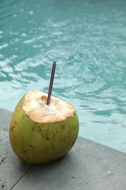 Yeşil hindistan cevizi, ferahlatıcı bir içecek ve açık havuzun yanında saman.