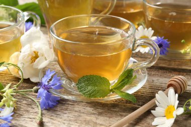 Cam bardaklarda aromatik bitki çayı, ahşap masada nane ve çiçekler, yakın plan.