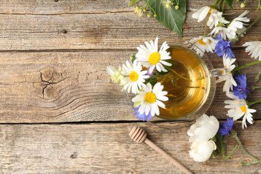 Cam bardakta Aromatik bitkisel çay, çiçekler ve ahşap masa, düz yatak. Metin için boşluk
