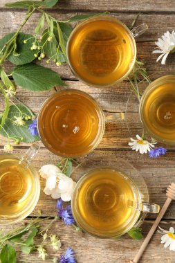 Cam bardaklarda Aromatik bitki çayı, çiçekler ve yeşil yapraklar ahşap masada, düz uzanmış