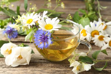 Cam bardakta Aromatik bitki çayı ve ahşap masada çiçekler, yakın plan.