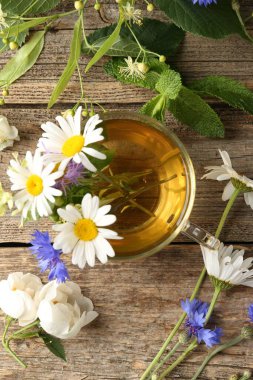 Cam bardakta Aromatik bitki çayı, tahta masada çiçekler ve yeşil yapraklar, düz uzanmış