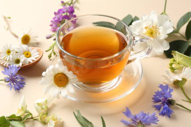 Cam fincanda aromatik bitki çayı ve bej arka planda farklı çiçekler, yakın plan.